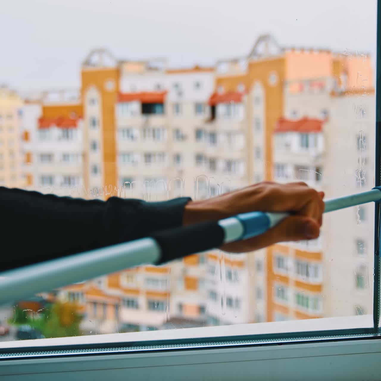Cleaning window with modern brush indoors. Worker washing window with a special brush on the background of multi-storey building