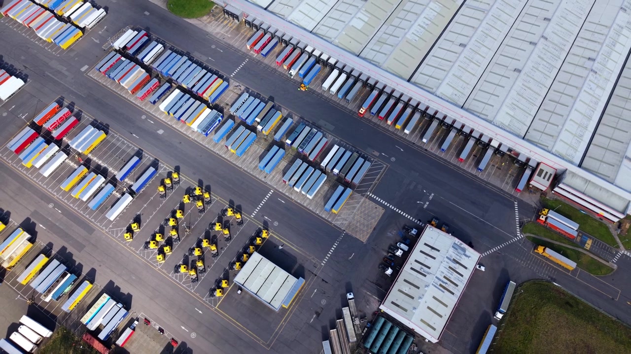 Massive logistics fulfillment hub with hundreds of freight trucks parked in precise geometric rows along extended shipping dock bays.