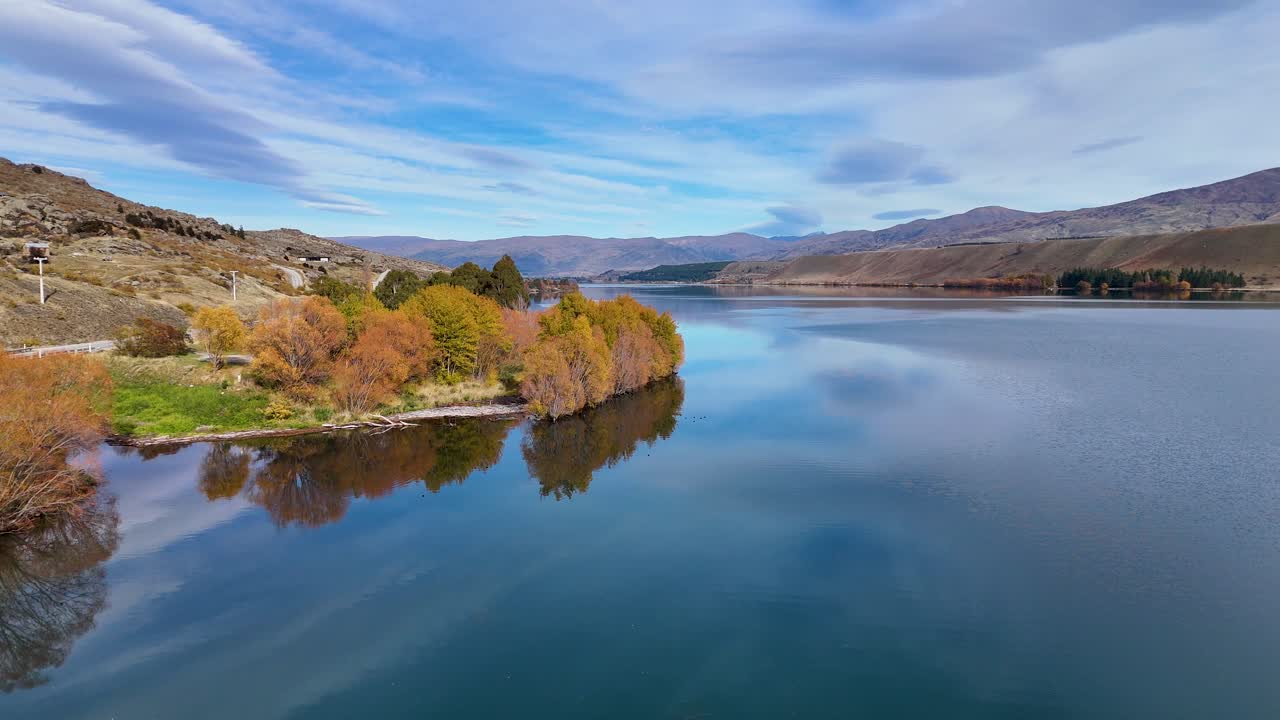 Drone captures serene autumn landscape over Lake Dunstan with vibrant foliage and calm waters under a clear sky