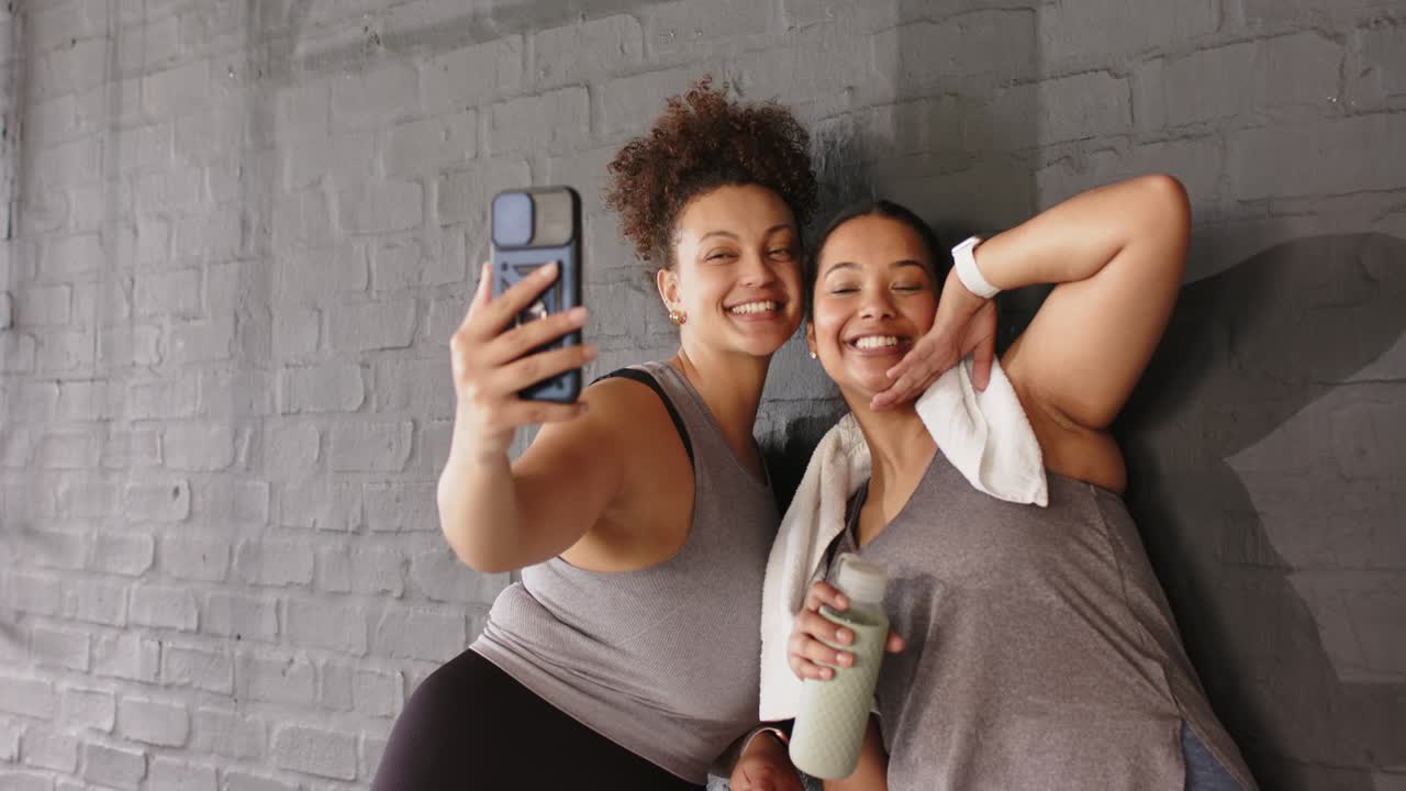 Dopo l'allenamento, diverse amiche si fanno dei selfie in palestra con lo smartphone e la borraccia