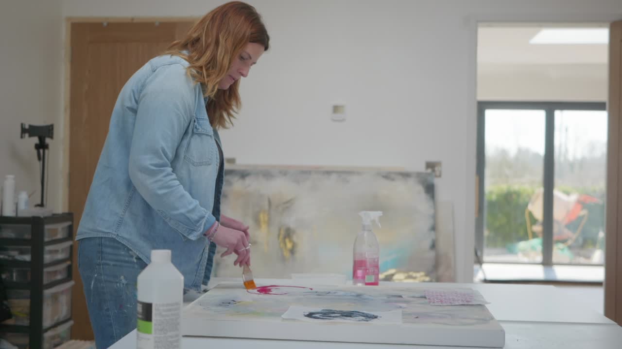 artista femenina cepillando pegamento en un activo de papel, en lienzo, en un estudio en casa