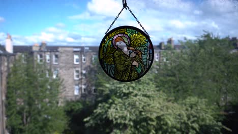 stain-glass pendant hanging in the window with the view of a backyard