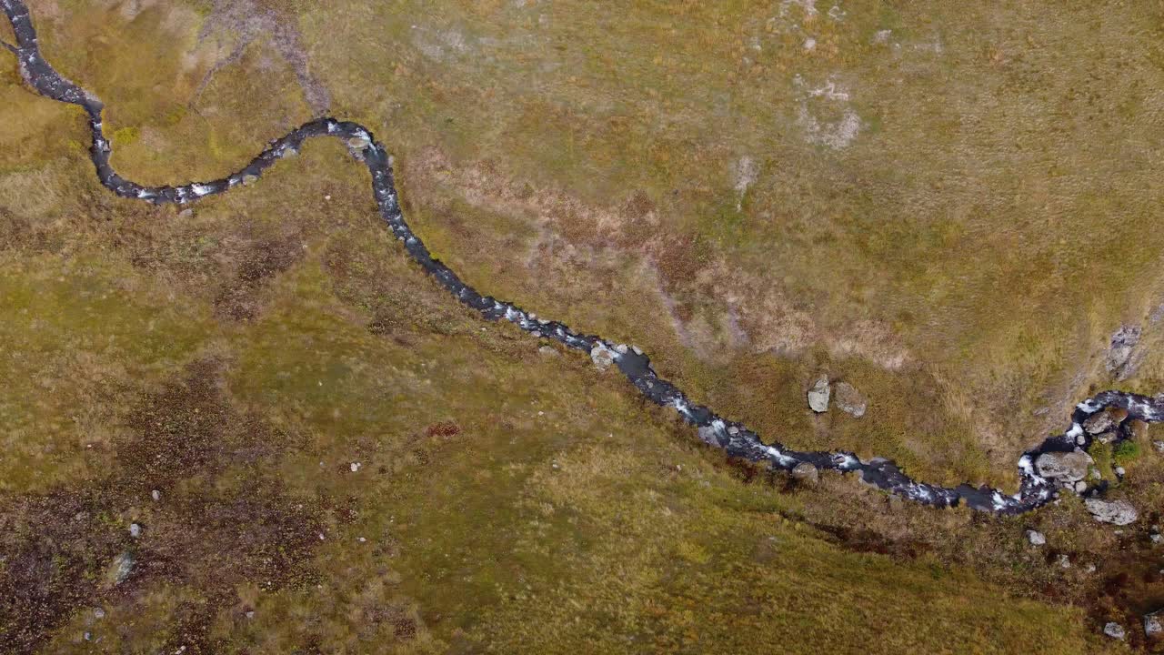 Top-down panning drone fly at small creek winding through countryside fields surrounded by bare hills, Khevsureti, Mtskheta-Mtianeti, Georgia