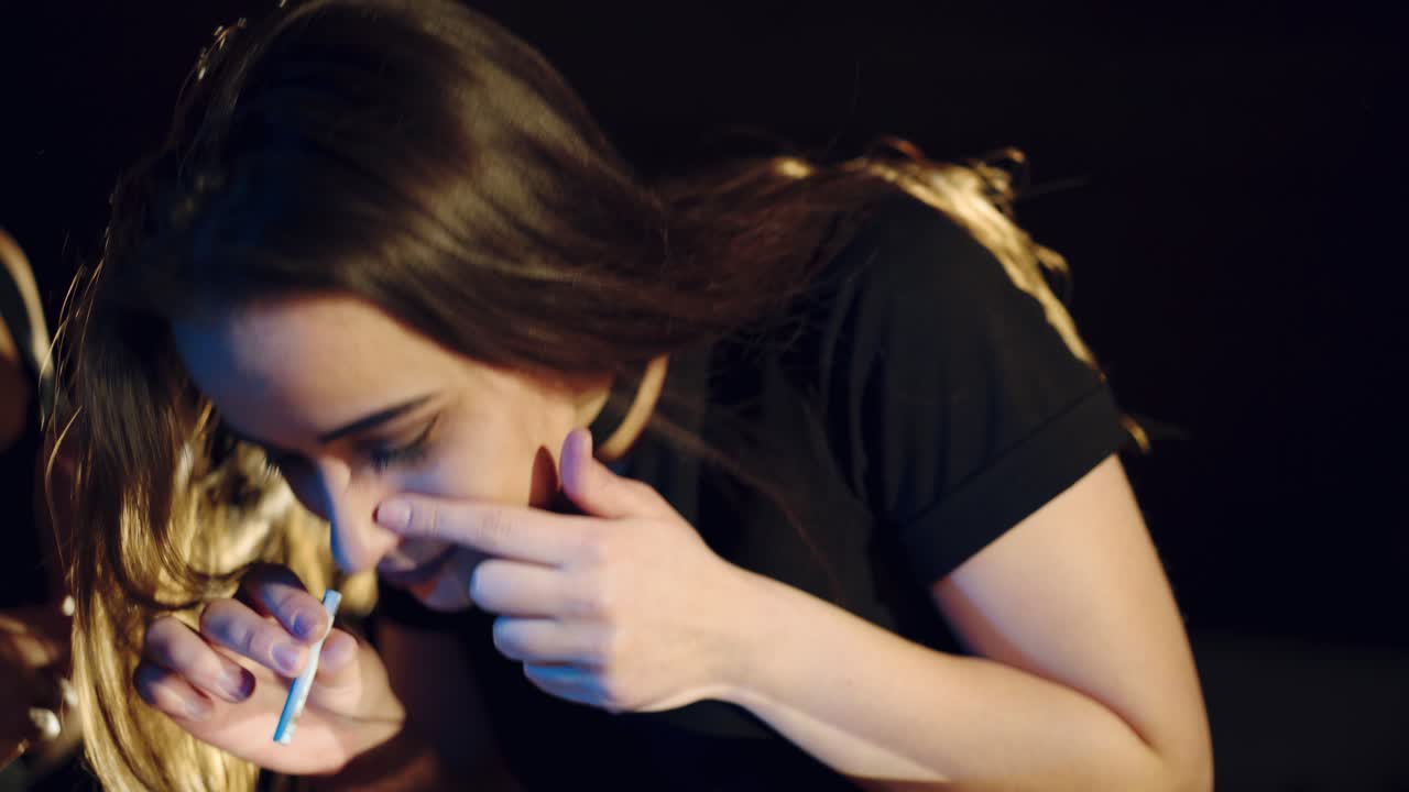 Two brunette girls snort cocaine on a mirror with a roll of banknotes. Social problems. Drug Abuse