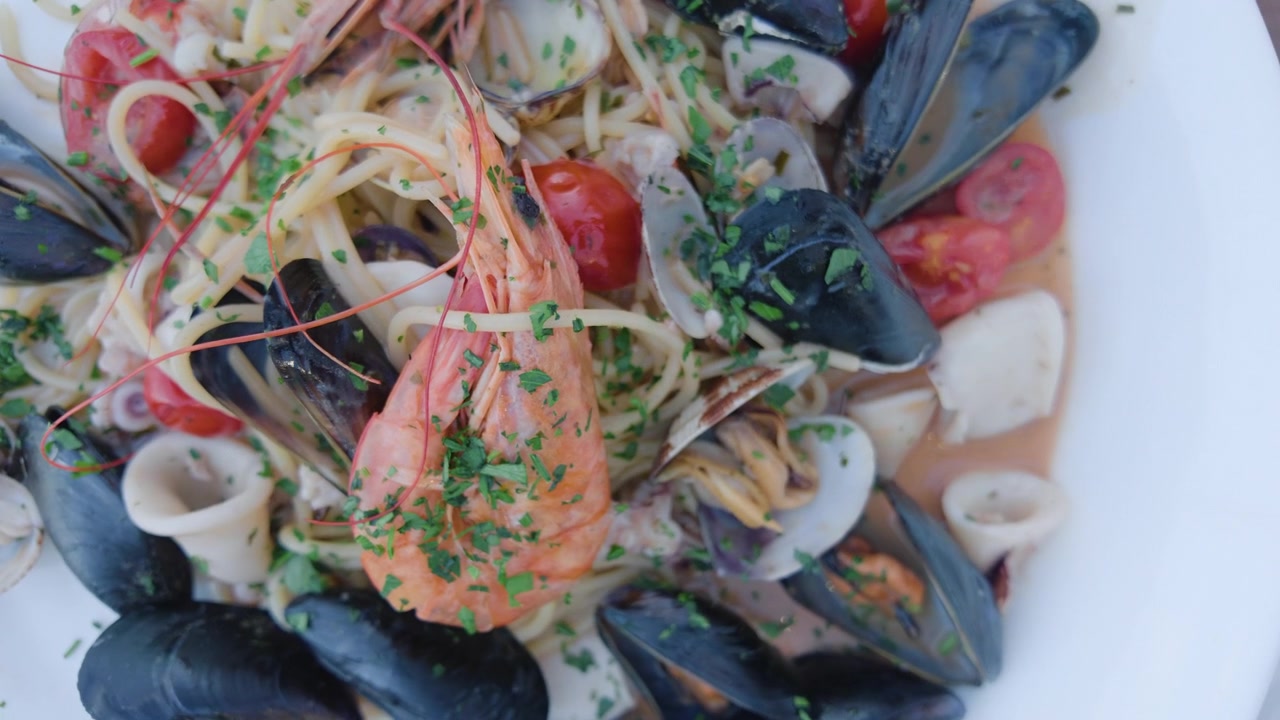 Close-up of a seafood pasta with mussels, clams, shrimp and cherry tomatoes on a white plate