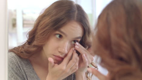 young woman removing contact lenses for eyes at mirror in home bathroom