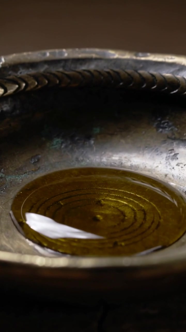 Video verticale: Dopo essersi depositata, una goccia dorata si espande a formare un disco in una ciotola di metallo con bordo intrecciato.