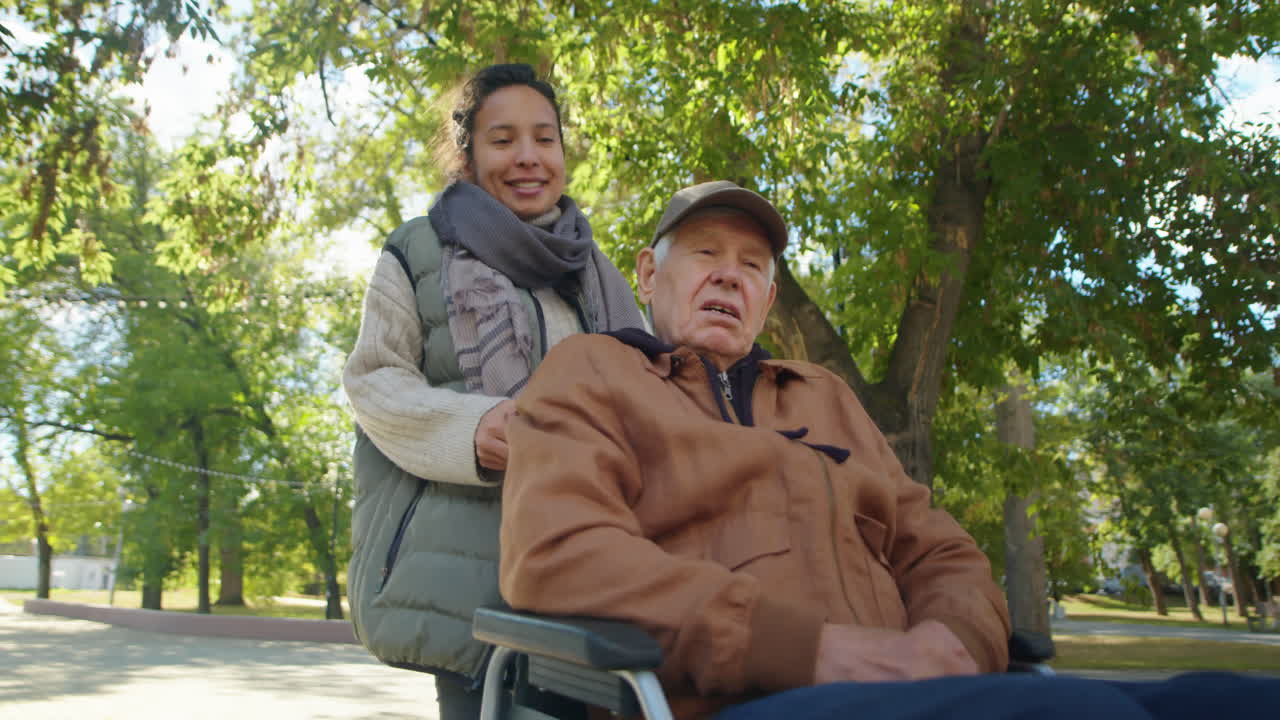 Caregiver assisting elderly man in wheelchair in park
