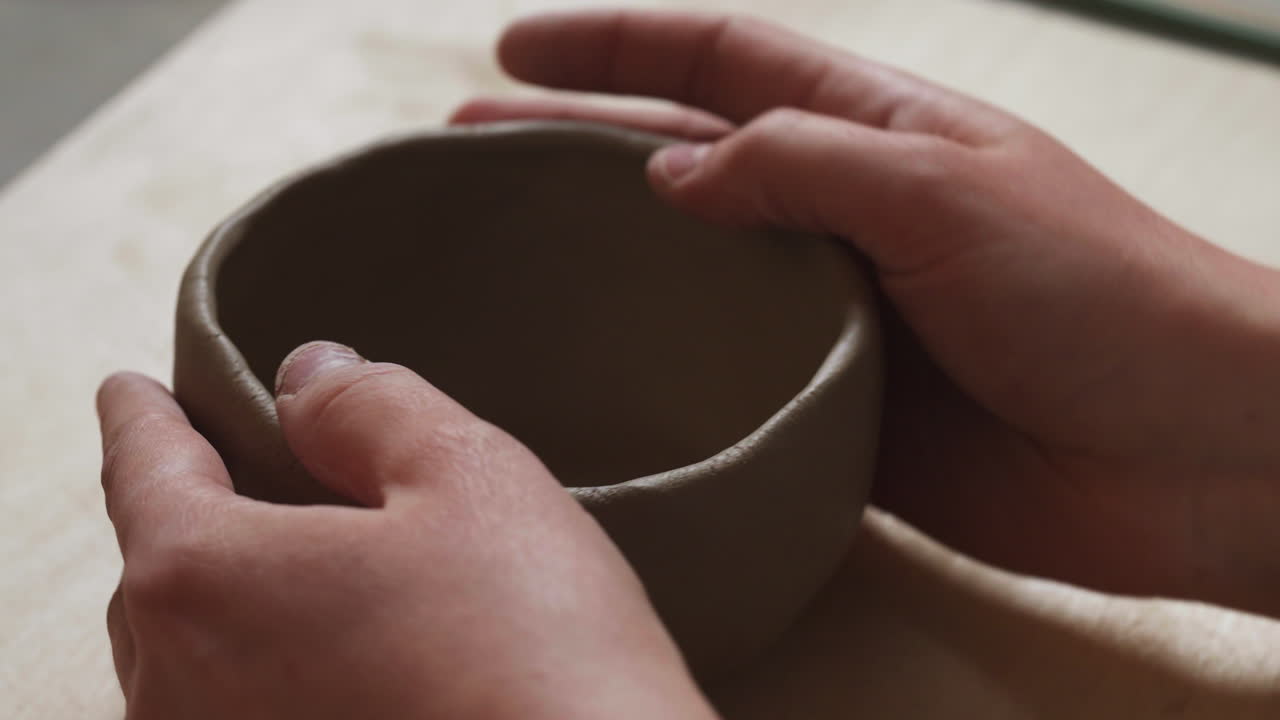 Close up shot of white hands making mug from clay with bare hands, interior