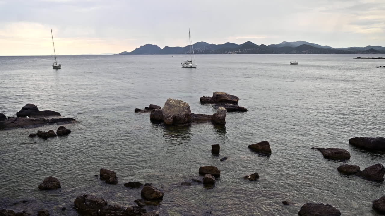 View of the Mediterranean sea rocky coast on the Island of Sainte-Marguerite, boats, town in the distance, France