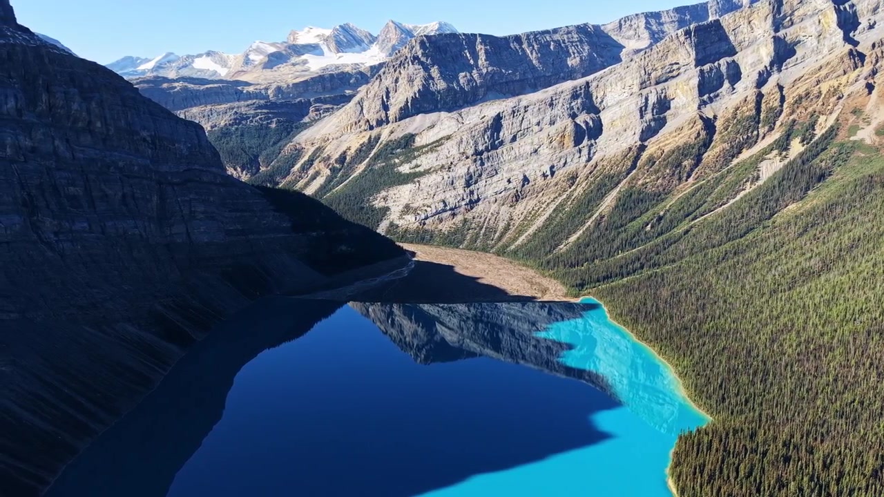 Vista aerea da drone di un lago turchese in una valle profonda che riflette ripide scogliere calcaree e cime innevate, Parco Nazionale di Banff, Canada