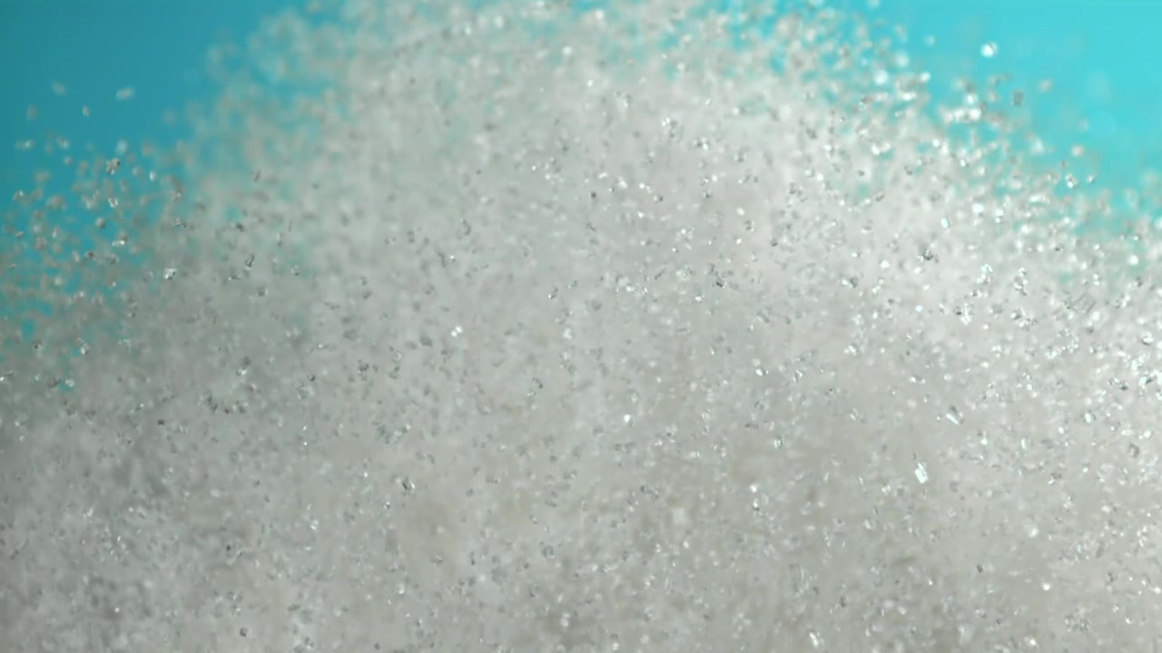 Esplosione dinamica di particelle di zucchero bianco su uno sfondo verde acqua.