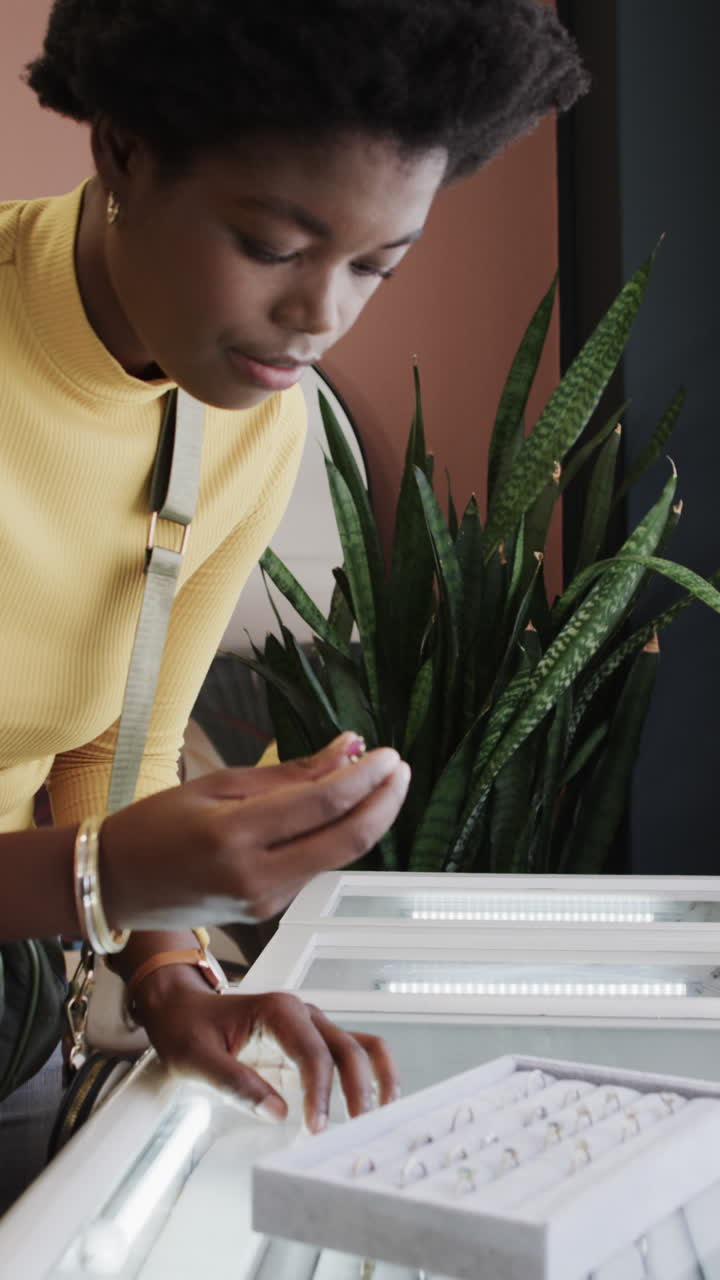Vertical video of african american woman choosing ring in jewellery shop in slow motion