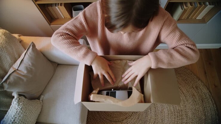 Lifting box flaps girl pulling tissue paper revealing black, white sneakers in living room