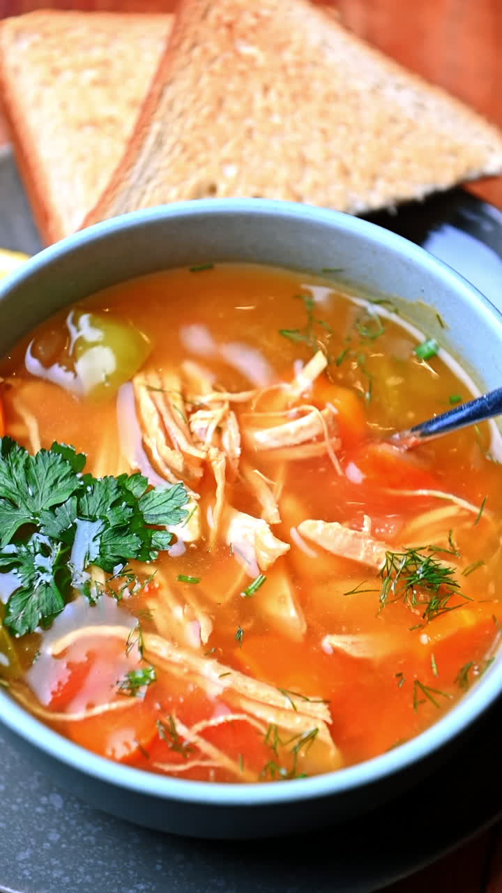 Chicken soup with herbs and toast on a wooden table. Warm chicken soup with vegetables and dill served with bread toast