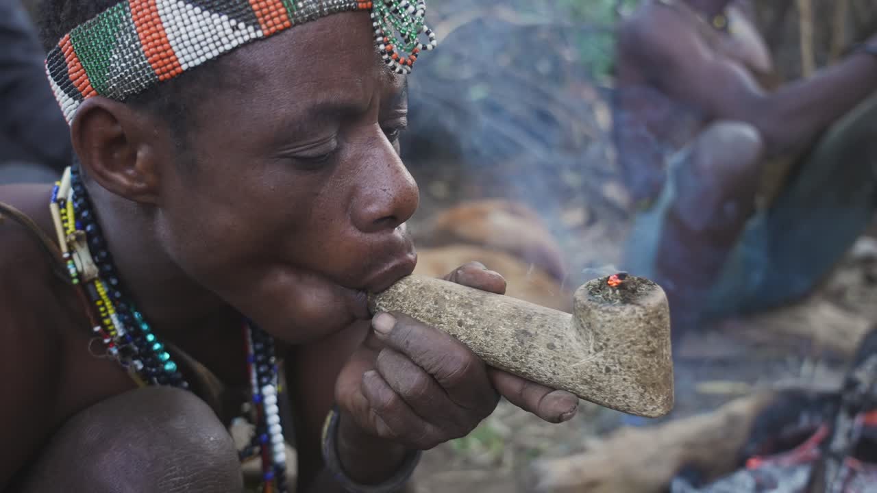 Cinematic close up shot of tribal african man smoking cannabis in a pipe. Traditional bushmen tribe, Tanzania, Africa 4K.