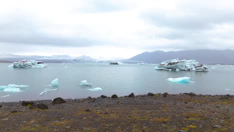 Aerial-dolly-past-a-tourist-looking-at-the-melting-icebergs-in-a-lagoon-in-Iceland