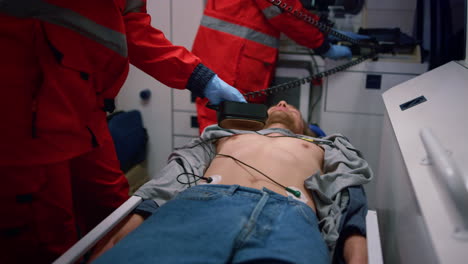 Emergency-medical-doctors-using-heart-defibrillator-on-patient-in-ambulance-car