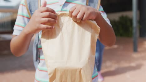 Video-midsection-of-african-american-schoolboy-holding-packed-lunch-outside-school