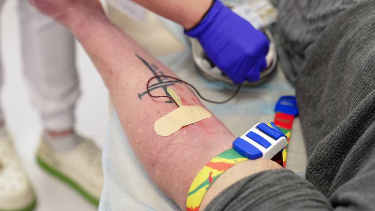 Catheter and thin tube is attached to the vein on the male hand. Medic in blue gloves puts an adhesive plaster on. Close up. Blood test. PRP therapy.