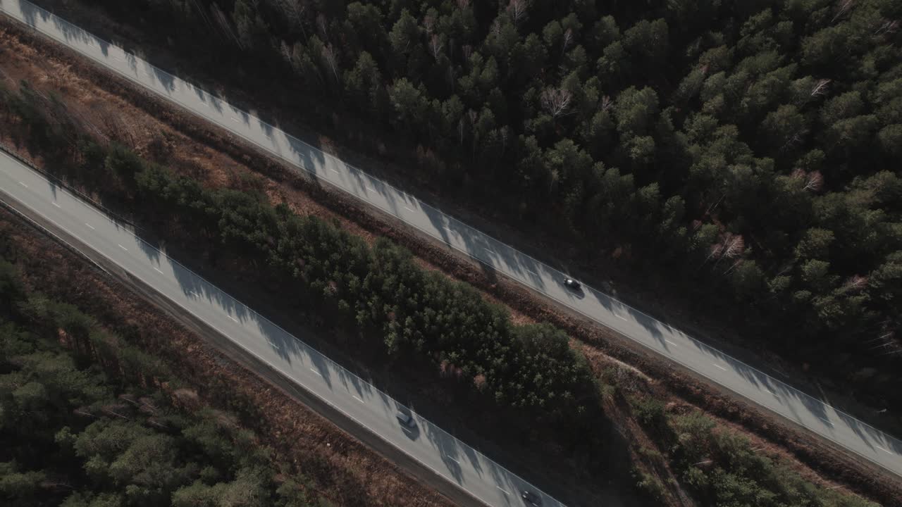 Vista drone di un'autostrada asfaltata che attraversa una fitta foresta con lunghe ombre e colori autunnali, mostrando l'infrastruttura di trasporto rurale nella regione degli Urali, Russia
