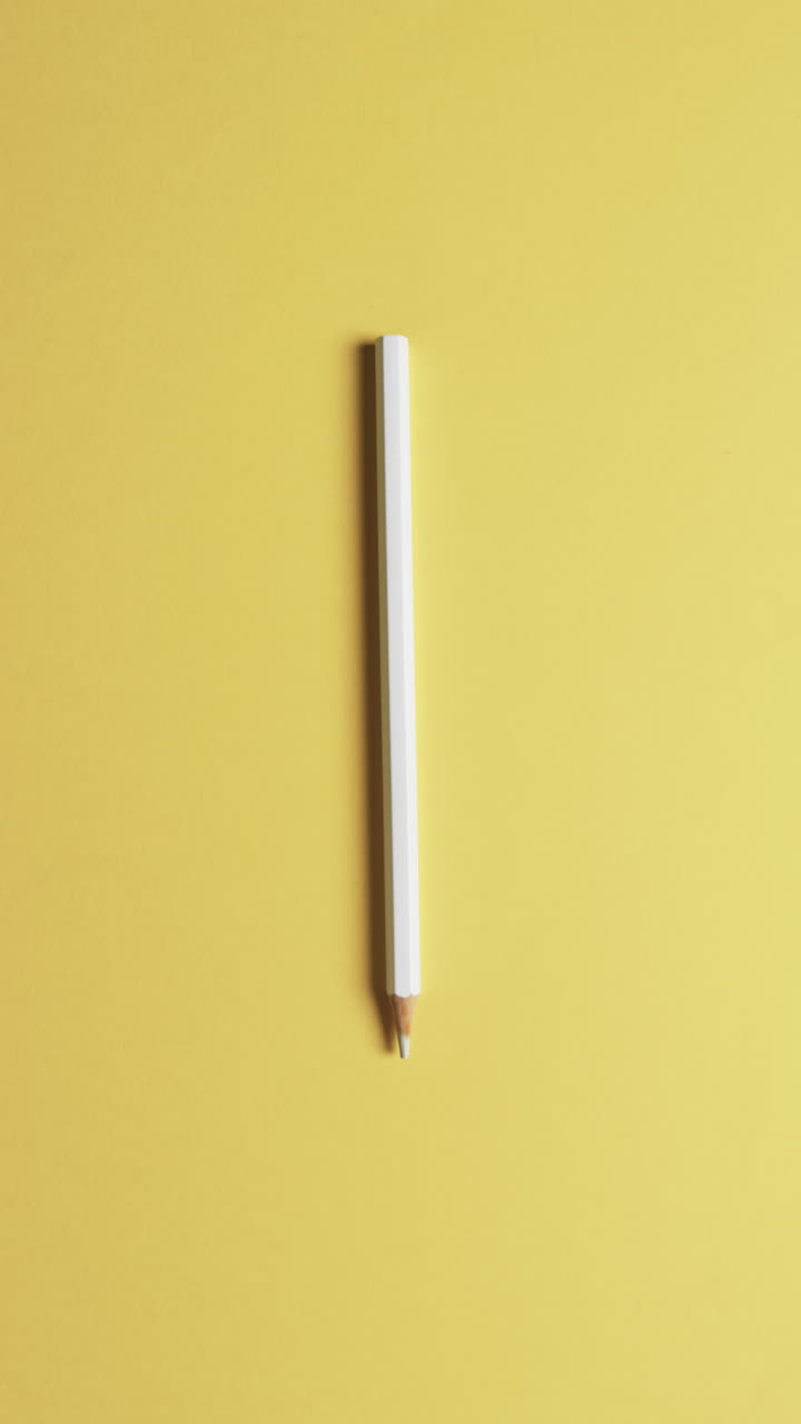 Vertical video of overhead view of yellow crayon on yellow background, in slow motion