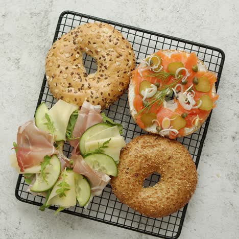 two delicious bagel sandwiches with ham and cheese  smoked salmon and various herbs and vegetables