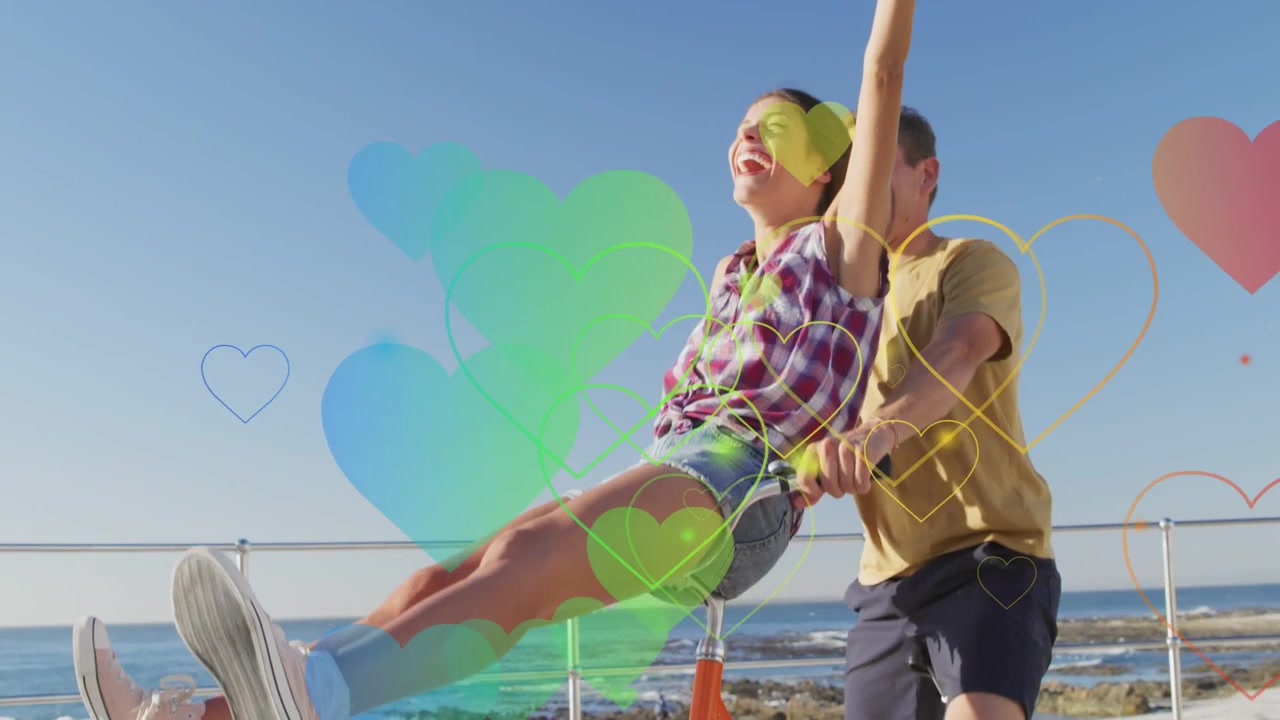 Una coppia romantica in bicicletta arancione vicino all'oceano, l'uomo pedala facendo apparire cuori fluttuanti scintillanti per uno spot di viaggio.