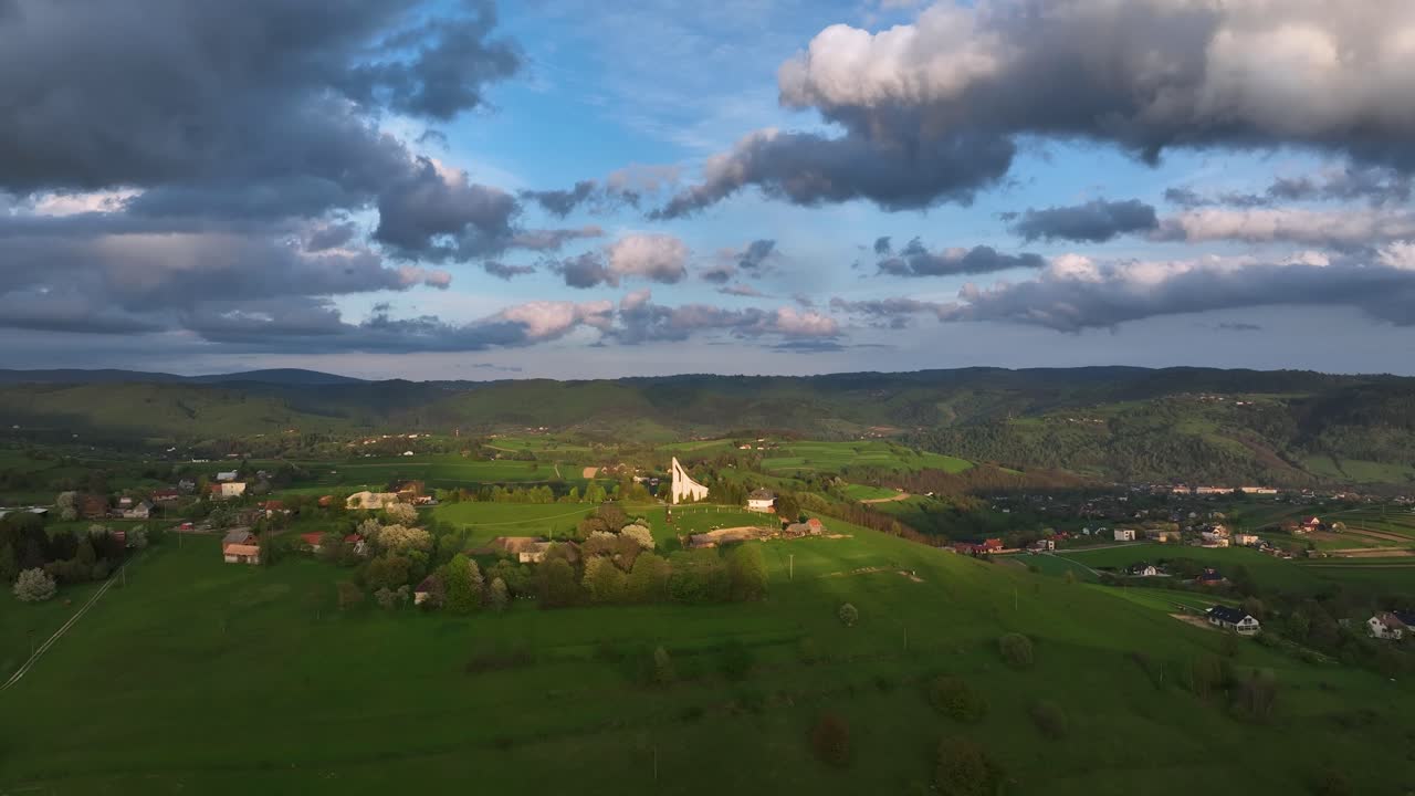 Divine Glow: Drone retreats, the sun's last rays illuminate the hilltop church, casting divine radiance in a shadowed countryside