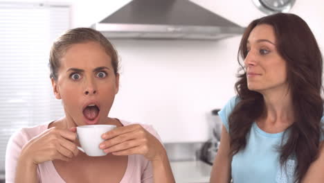 woman whispering gossips to a friend holding a cup of coffee