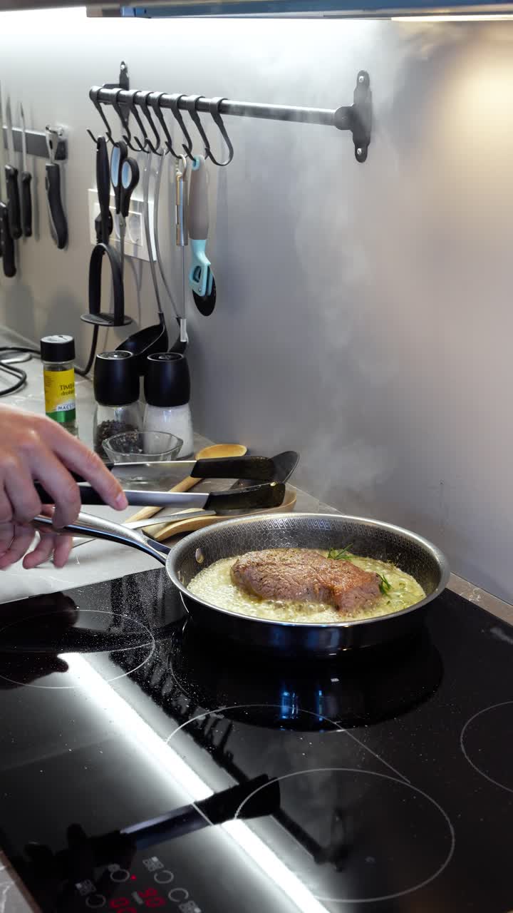 Close-up of ribeye steak pan-frying in a professional kitchen pan, sizzling in butter with seasoning added for flavor