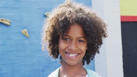 Portrait-of-happy-african-american-schoolgirl-with-climbing-wall-in-background