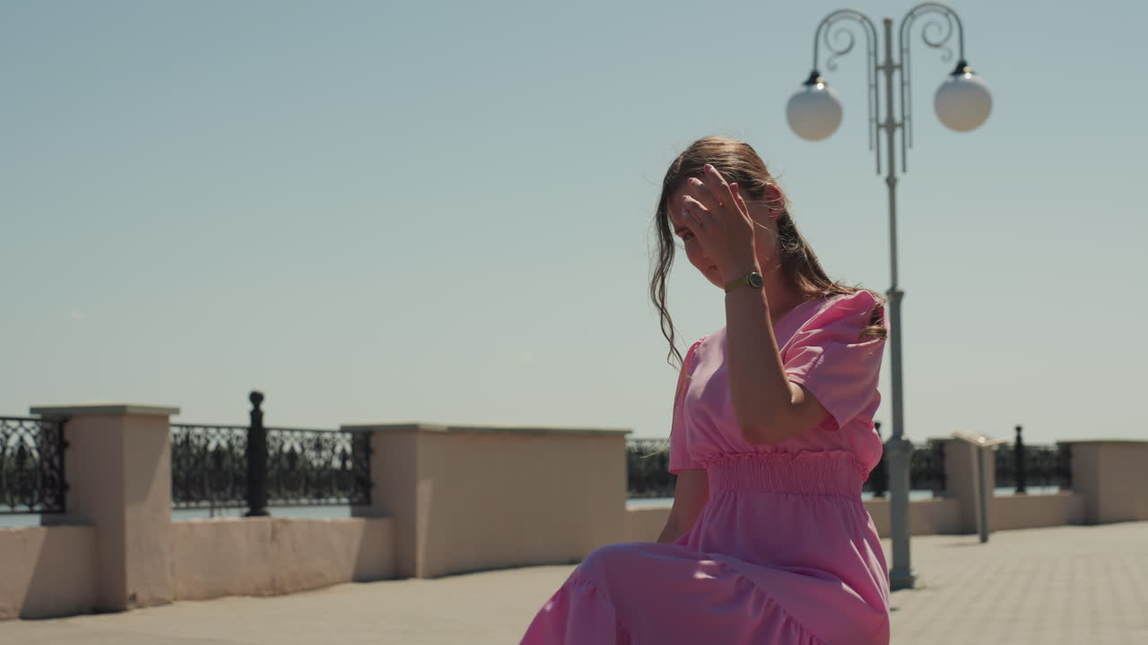 Garota com tranças aproveitando a luz do sol, mulher vestida de rosa olhando pensativamente para as flores, jovem senhora de vestido rosa claro sentada em um banco de pedra perto de flores coloridas e poste de luz