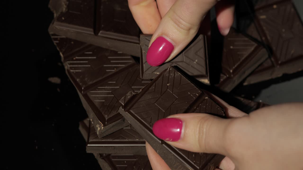 una mujer rompe una barra de chocolate negro. un primer plano de los dedos de una mujer.