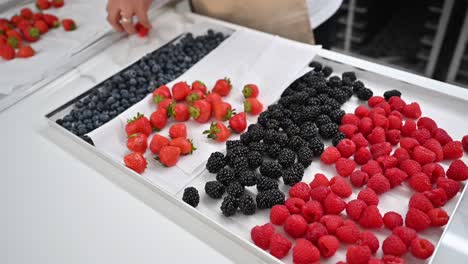 ein bäcker organisiert frische beeren, die für kuchen- und muffin-toppings in einer örtlichen bäckerei ausgestellt werden