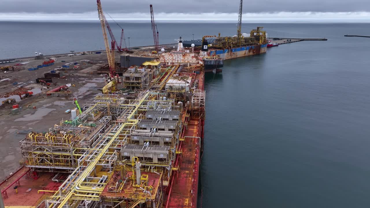 Drone footage of a rusted red tanker moored at the quay, undergoing dismantling for scrap. Industrial ship recycling in progress from an aerial perspective.