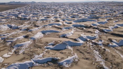 little yellow sahara desert and sand dunes partly covered with white snow with small mountains at the horizon on a bright cold winter day