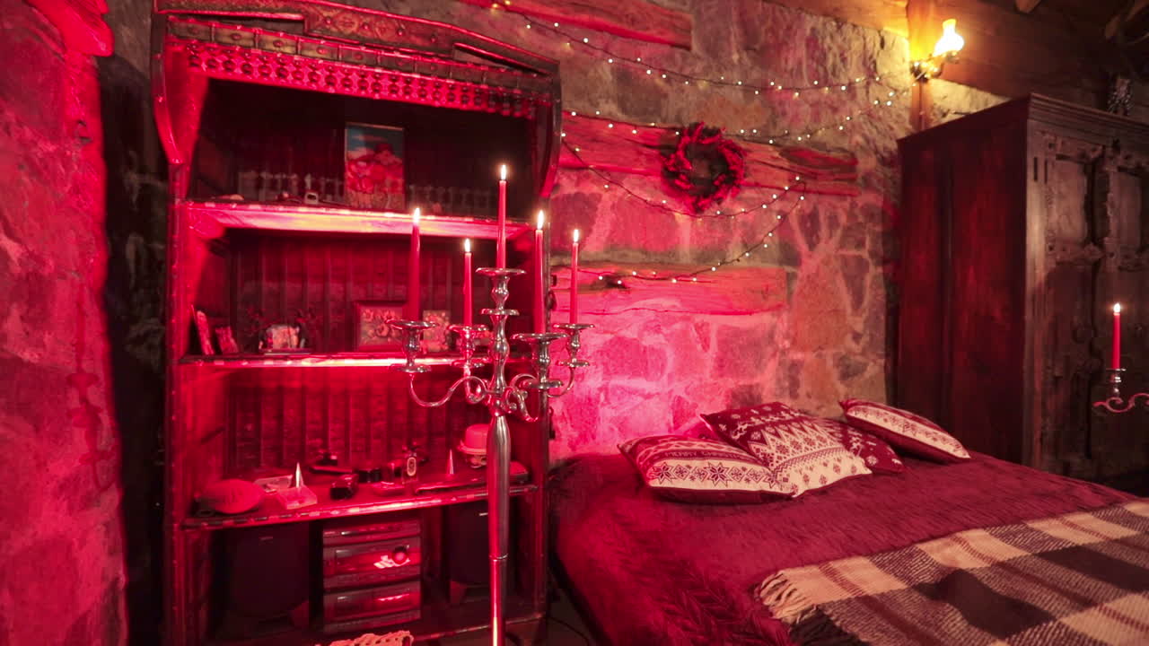 Cozy bedroom made in medieval style with Christmas decorations. Big bed among two pieces of furniture and long candlesticks lit in red light.