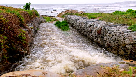 Regenwasserabfluss-Sprudelt-Aus-Dem-Regenwasserabfluss-Mit-Gabionenwänden-In-Richtung-Meer