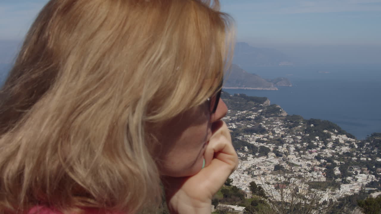 Beautiful woman relaxes at mountain top, smells flower, looks at capri italy