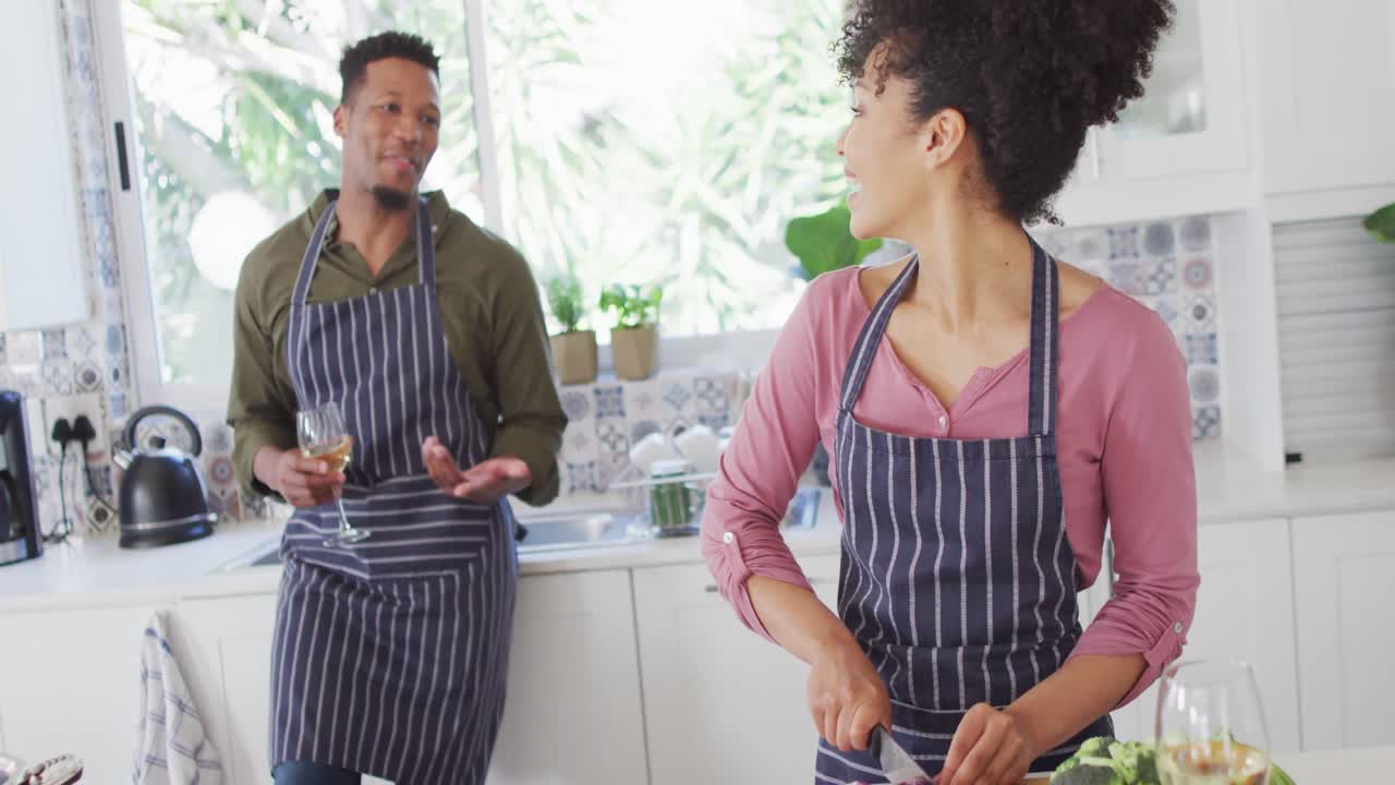 feliz pareja afroamericana cocinando y bebiendo vino en la cocina