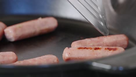 spatula stirring sizzling breakfast sausage with grill marks in cast iron pan in slow motion