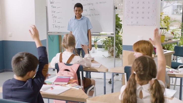 Student Standing In Front Of Blackboard In English Classroom Chooses A Redheaded Classmate Who Has His Arm Raised