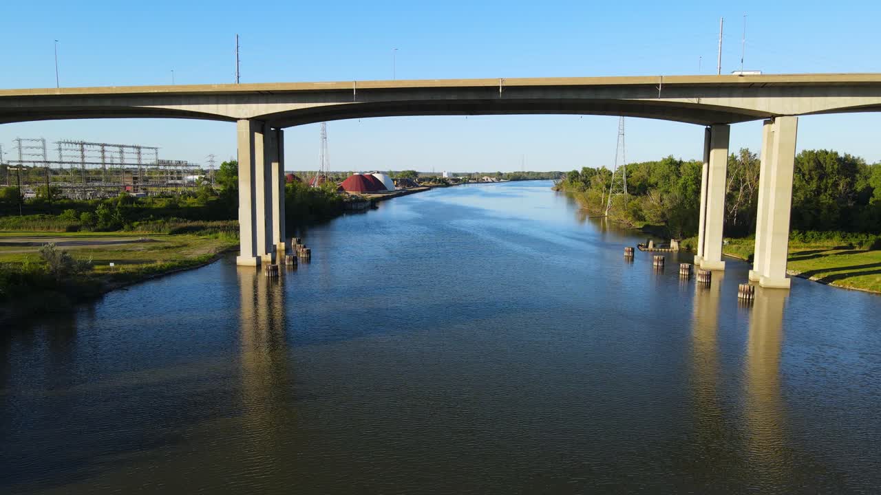 Deep blue river and highway bridge above, aerial fly under view