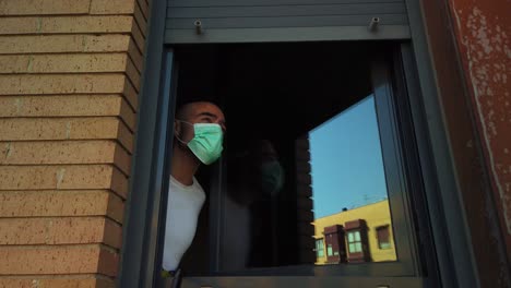 a shot of a man lening out the window, taking off a disposable mask and taking deep breaths