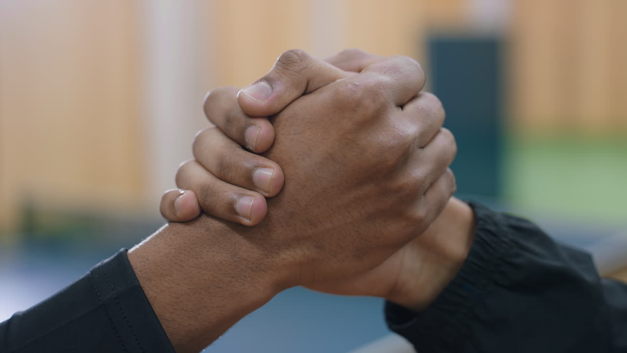 Close up hand view of two people firmly shaking hands indoors against blurred background representing unity respect teamwork determination partnership