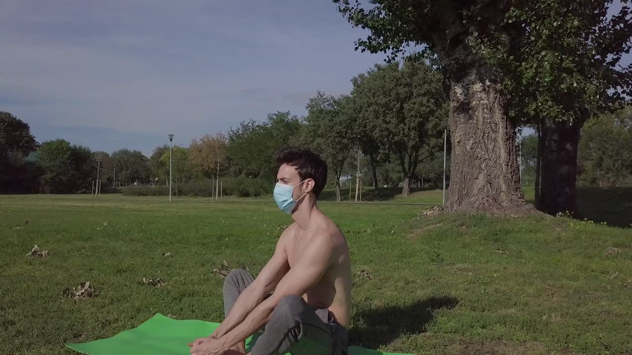 persona masculina con máscara haciendo una simple postura de yoga en el parque
