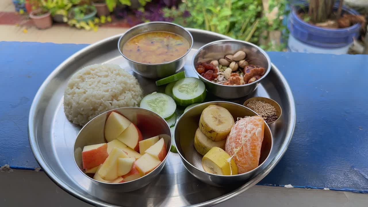 Spinning shot of a healthy Indian thali served with rice, dal, fruits, nuts, and seeds on a stainless steel plate, representing balanced diet and traditional Indian cuisine