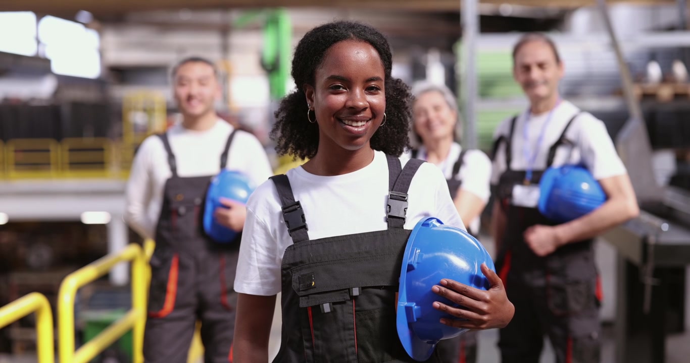 Smiling Female Factory Worker Standing with Colleagues in Industrial Warehouse