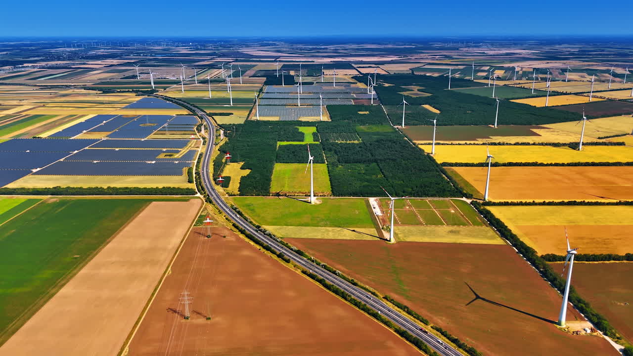 Wind and solar energy scene. An aerial view displays vast fields of wind turbines and solar panels among green and brown agricultural patches
